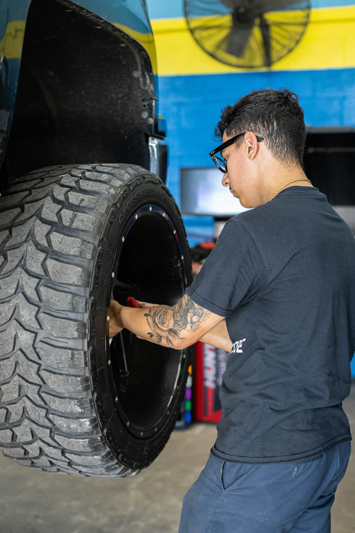 A technician handling a tire and wheel assembly beside a vehicle in a workshop